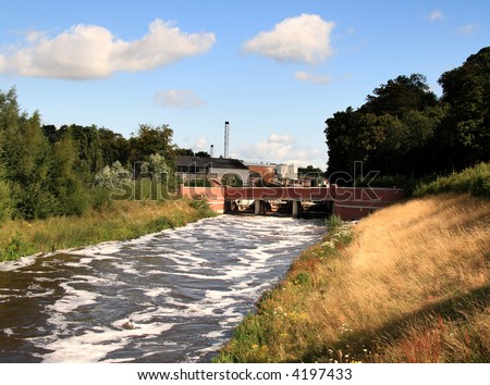 Sluice Gate controlling the flow of a swollen River with a Factory in the background