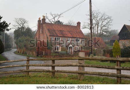 Winter scene of a Farmhouse and outbuildings in an Hamlet in Rural England with a wooden fence in the foreground
