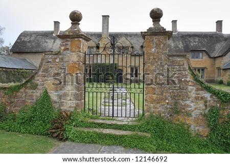 Gated entrance to a Medieval natural stone Thatched English Village Manor House and garden with a wall and gate to the front