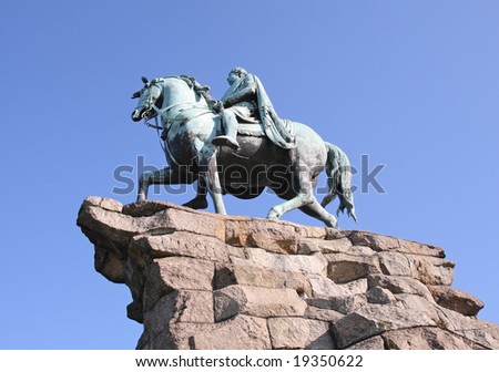 Copper Statue of a Horse and Rider on a Rocky Plinth  in an English Park against a clear Blue Sky