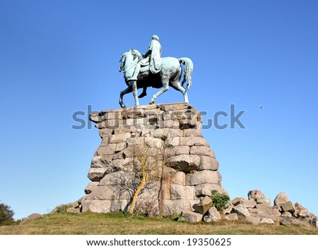 Copper Statue of a Horse and Rider on a Rocky Plinth  in an English Park against a clear Blue Sky