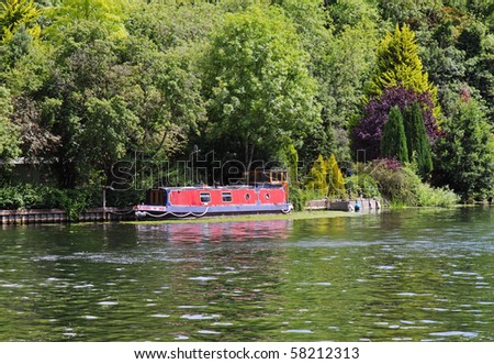 Moored Narrow-boat on the Banks of the River Thames in England with Wooded hillside behind
