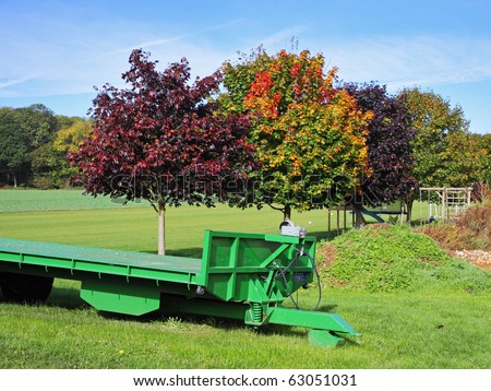 A Row Beech and Maple Trees in Autumn colors in Rural England with a Farm Trailer in the foreground