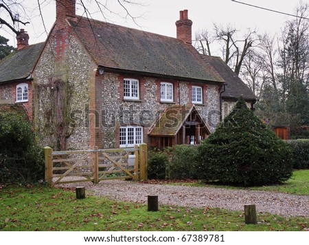 A Traditional English Village Brick and Flint House with hedge and gate to the front