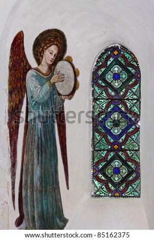 Stained Glass window in a medieval English Church with wall painting of an Angel to the side