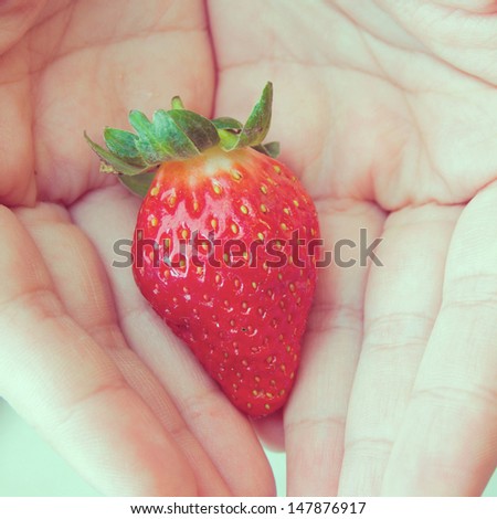 one fresh strawberry in hands with retro filter effect