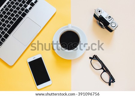 Creative flat lay photo of workspace desk with laptop, smartphone, coffee, eyeglasses and film camera on yellow modern background
