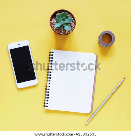 Creative workspace desk with notebook, smartphone, pencil and cactus on yellow background