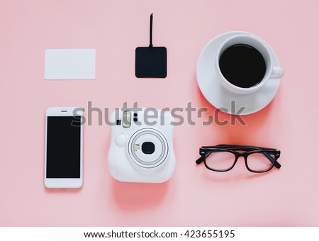 Creative flat lay photo of workspace desk with instant camera, coffee, tag, smartphone and eyeglasses on pink background, minimal and modern design with copyspace for background