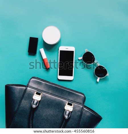 Fashion concept : Flat lay of black leather woman bag open out with cosmetics, accessories and smartphone on green background