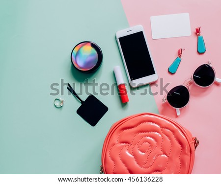 Flat lay of pink cute woman bag open out with cosmetics, accessories, tag card and smartphone on colorful background with copy space