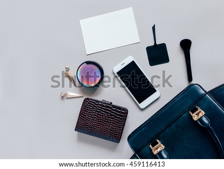 Fashion concept : Flat lay of black leather woman bag open out with cosmetics, accessories, wallet, smartphone and blank card of paper on grey background with copy space
