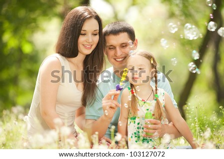 Happy mother, father and daughter blowing bubbles in the park