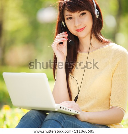 Cute woman in earphones with white laptop in the park