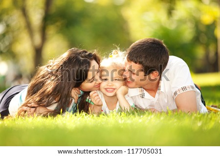 Happy mother and father kissing their daughter in the park Happy mother and father kissing their daughter in the park