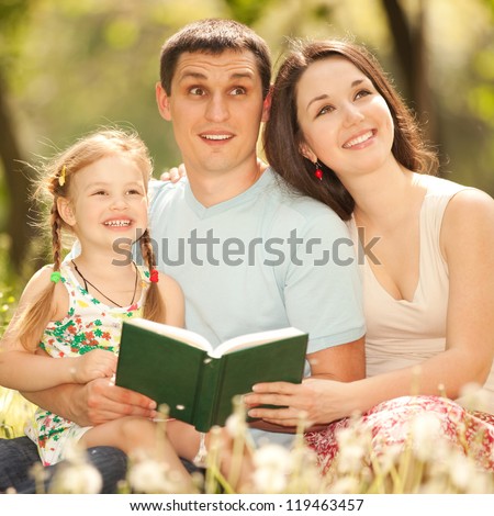Happy mother, father and daughter read a book in the park