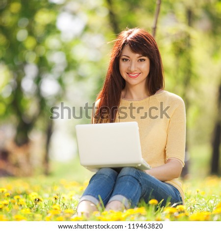 Cute woman with white laptop in the park with dandelions