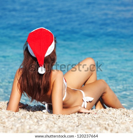 Young woman in santa hat sitting on the beach. Christmas vacation