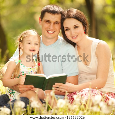 Happy mother, father and daughter read a book in the park