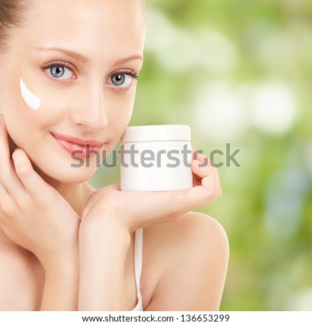 Cute woman applying cream to her face
