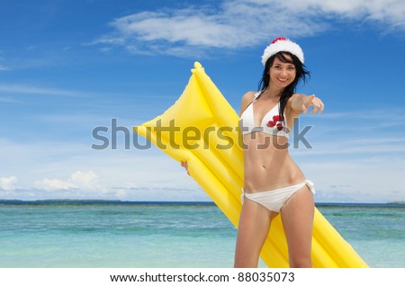 Happy santa woman with inflatable mattress on the beach. Christmas vacation