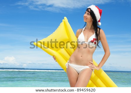 Happy santa woman with inflatable mattress on the beach. Christmas vacation