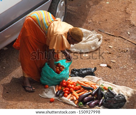 KAMPALA, UGANDA - SEPTEMBER 28, 2012.  An African woman bends over to organize her for sale vegetables in the taxi park in Kampala, Uganda on September 28,2012.