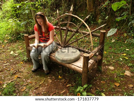 A caucasian girl reads a book while sitting on a wooden bench in the forest