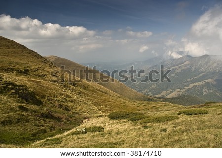 Sunny day at the mountain called Balkan. There is dark gradient in the upper sky and clouds over mountain tops. Yellow green color of grass.