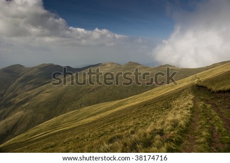 Sunny day at the mountain called Balkan. There is dark gradient in the upper sky and clouds over mountain tops. Yellow green color of grass. Image converted from RAW file for best tonal range.