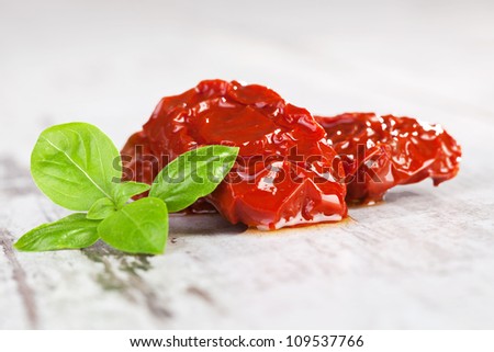 Luxurious dried tomatoes with fresh basil leaves on white wooden textured background. Mediterranean traditional cooking.