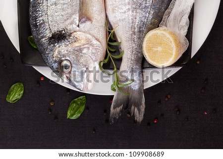 Luxurious delicious seafood concept in black and white. Two sea bream fish on black and white plate, detail on head and tail with lemon, fresh herbs and peppercorn.