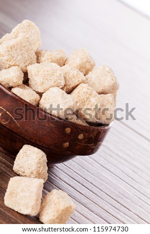 Brown sugar cubes in wooden bowl on brown background. Bright natural sugar background.