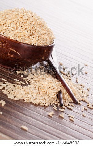 Brown rice background. Rice in wooden round bowl with chopsticks on brown background. Culinary natural rice eating.
