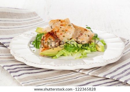 Healthy eating. Grilled fish fillet with fresh rocket salad, lettuce and avocado on white plate on white wooden textured background.