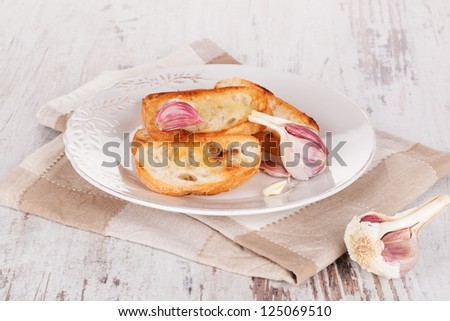 Baguette with garlic on white plate on white wooden textured background. Luxurious food background.