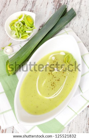 Delicious leek soup in white bowl with fresh and cut leek on white wooden background. Culinary healthy eating, top view.