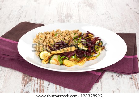 Culinary vegetarian eating. Couscous with fried vegetable beet and zucchini on white plate on white wooden textured background.