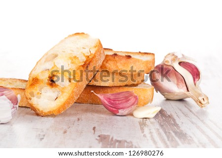 Luxurious garlic bread background. Roasted crunchy baguette with fresh garlic on white wooden textured background. Culinary healthy eating.