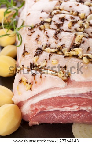 Pork belly background with fresh herbs, potatoes and onion on sheet pan ready to bake. Culinary meat eating.