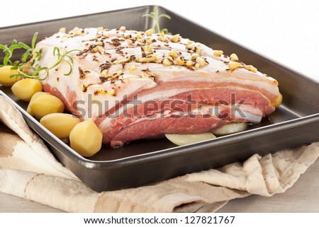 Delicious raw pork belly with fresh herbs and potatoes on baking tray. Luxurious meat eating.