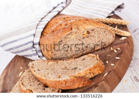 Dark wholesome bread and slices on round wooden kitchen board on white wooden textured background, rustic styles. Culinary delicious bread eating.