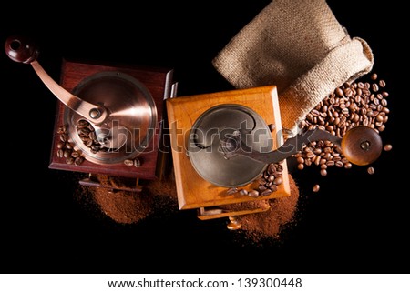 Two old vintage coffee grinder, sack with roasted coffee beans and ground coffee isolated on black background. Culinary aromatic coffee drinking.