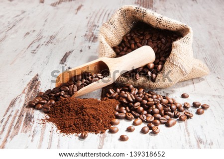 Coffee. Coffee beans in sack, ground coffee and wooden spoon on white wooden background. Culinary gourmet coffee drinking.