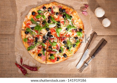 Round colorful pizza with ham, cheese, black olives, onion and various herbs on brown background, top view. Culinary pizza eating, rustic country style.