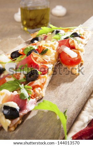 Culinary pizza eating. Pizza with prosciutto, ham, black olives, herbs on wooden cutting board on brown background. Traditional pizza background.