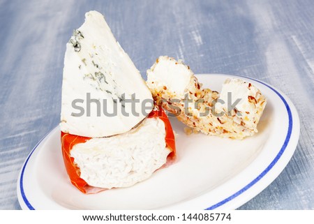 Luxurious colorful cheese assortment. Blue cheese, cream cheese and goat cheese on plate on blue wooden background. Culinary cheese eating.