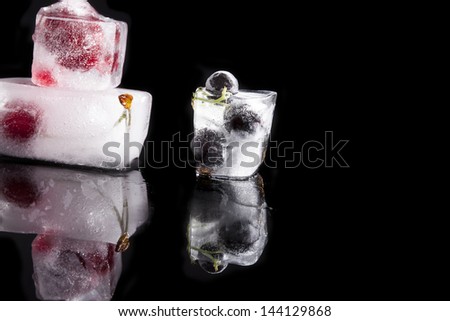 Ice cubes with fruit isolated on black background with reflection. Cherry, blackcurrant and strawberry frozen in ice blocks. Fresh luxurious fruit still life.