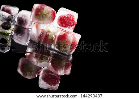 Frozen fruits in ice cubes isolated on black background. Luxurious dark glamour summer fruit background with copy space. Raspberry, strawberry and blackcurrant.