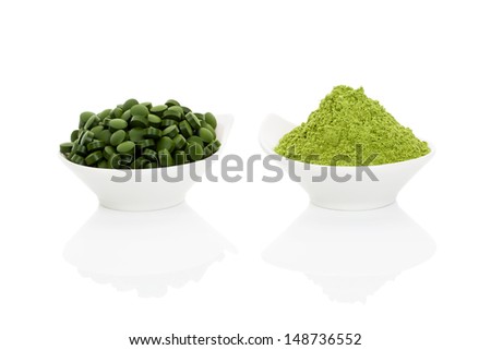 Wheat grass powder and green chlorella pills in two bowls isolated on white background. Alternative herbal medicine.